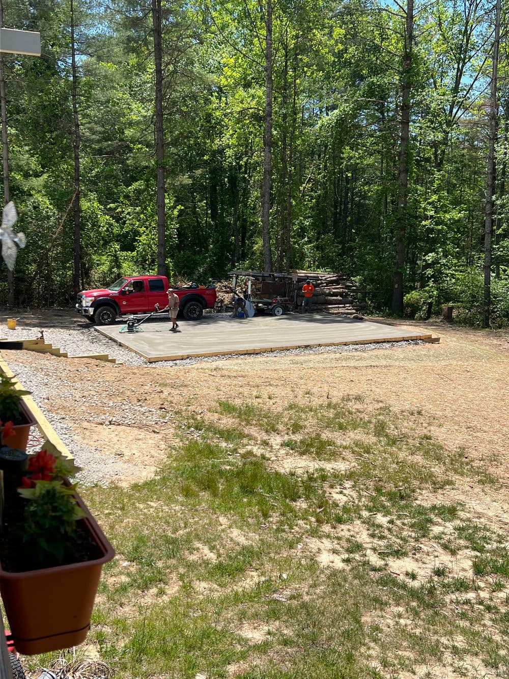 Construction crew pouring concrete slab for a patio in a wooded backyard setting.