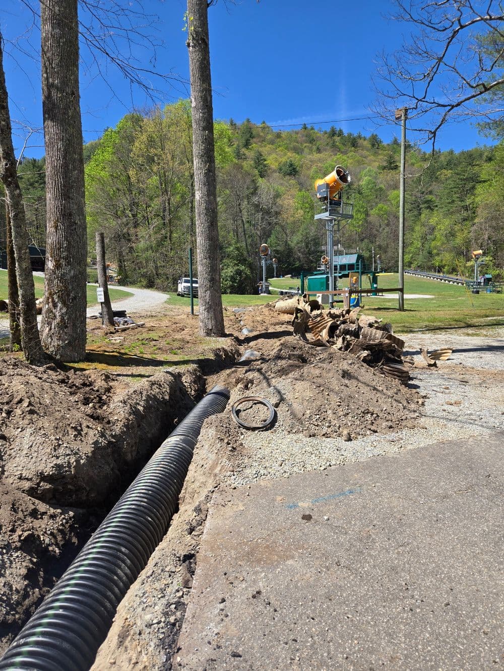 Construction site with exposed drainage pipe and trees, set against a mountainous background.