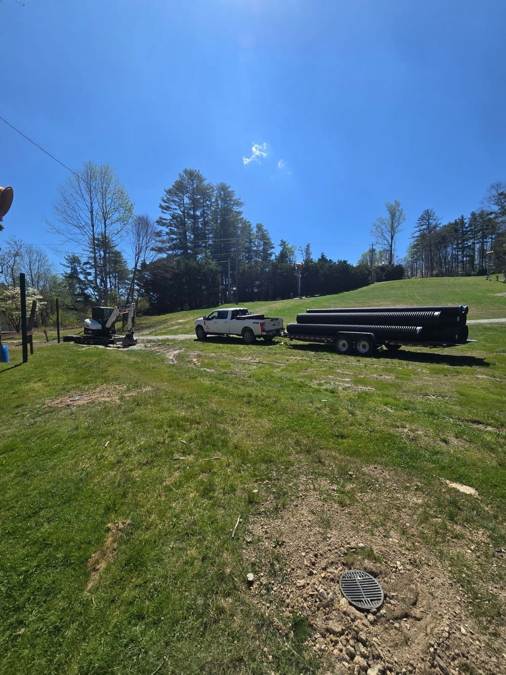 Truck with trailer carrying pipes on a sunny day in a grassy landscape.