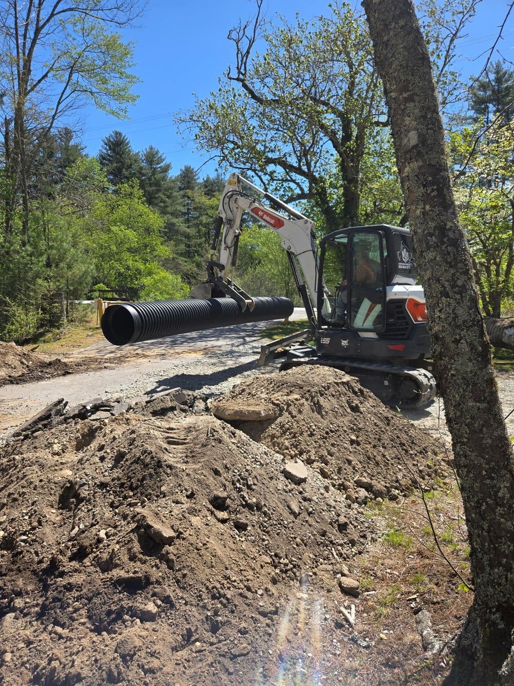 Excavator lifting black drainage pipe on a construction site surrounded by piles of dirt.