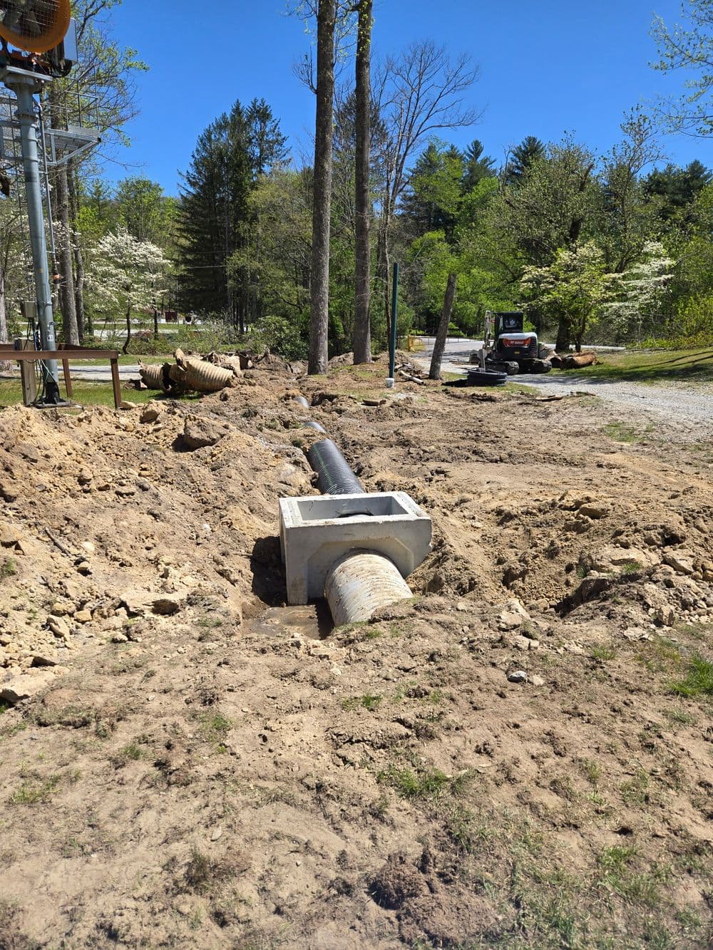 Excavated trench with drainage pipe installation in a rural landscape under clear blue skies.