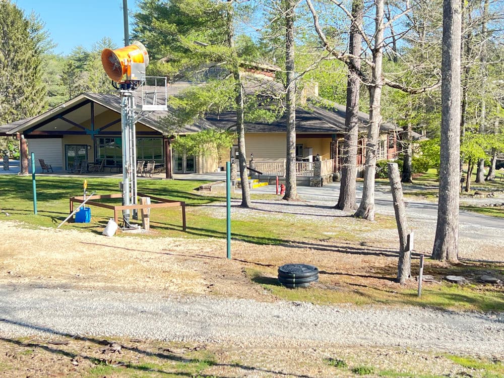 Lodge building with modern architecture surrounded by trees and gravel paths. Sunny day outdoors.
