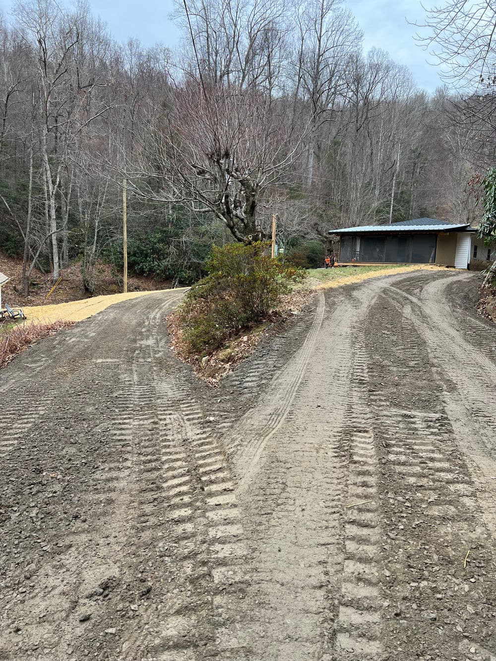 Dirt road intersection in wooded area with tire tracks and a cabin in the background.