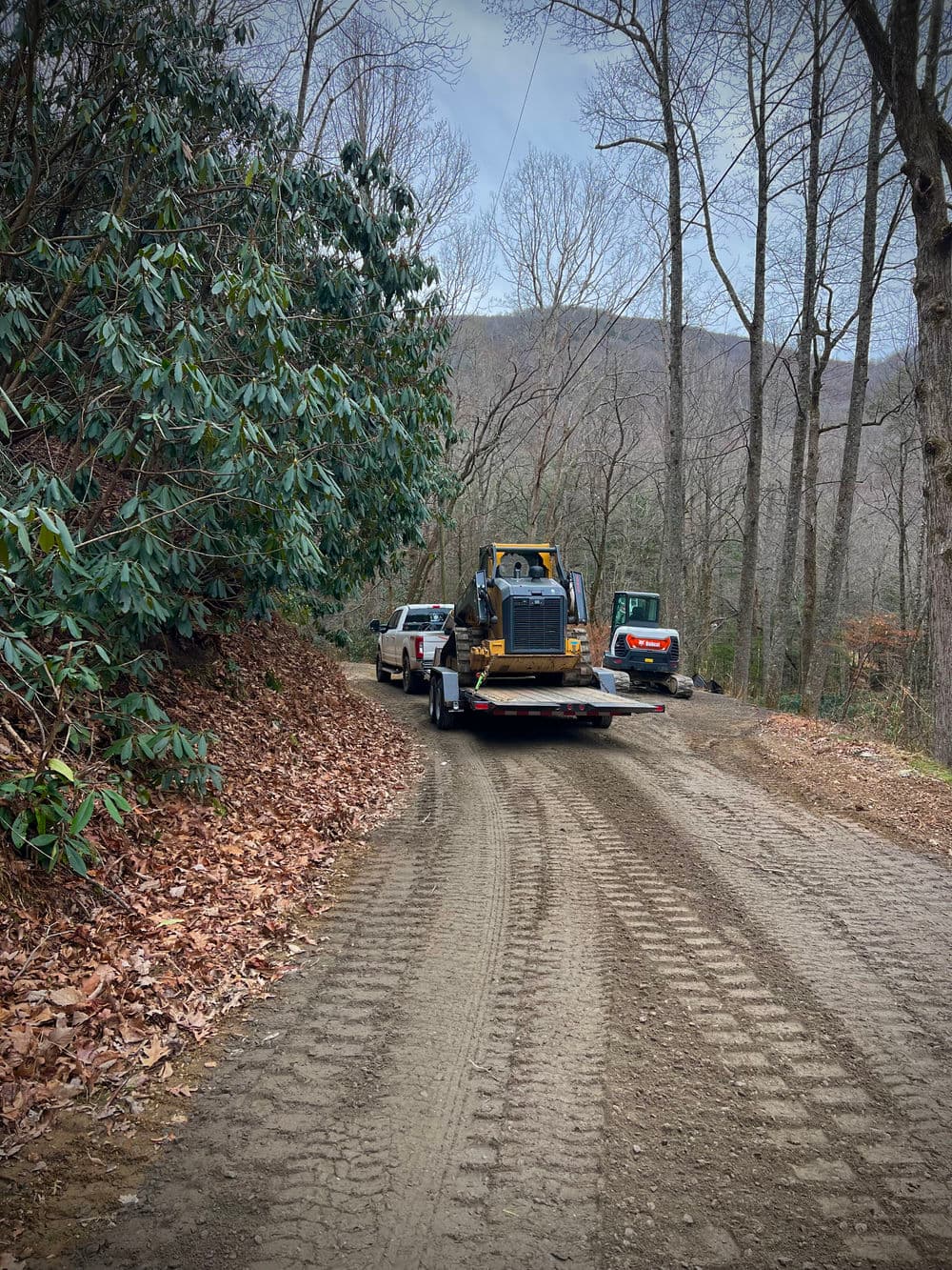 Construction vehicles on a gravel road surrounded by trees in a wooded area.