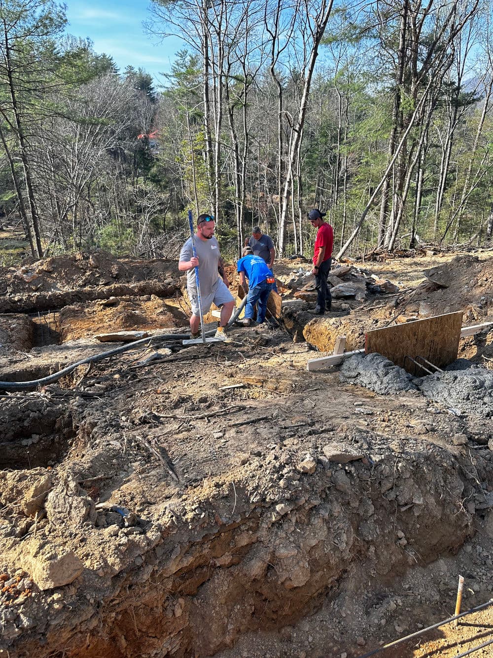 Construction workers digging in a forested area, preparing for a building foundation.