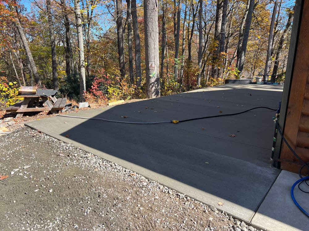 Freshly poured concrete driveway surrounded by autumn trees and natural setting.