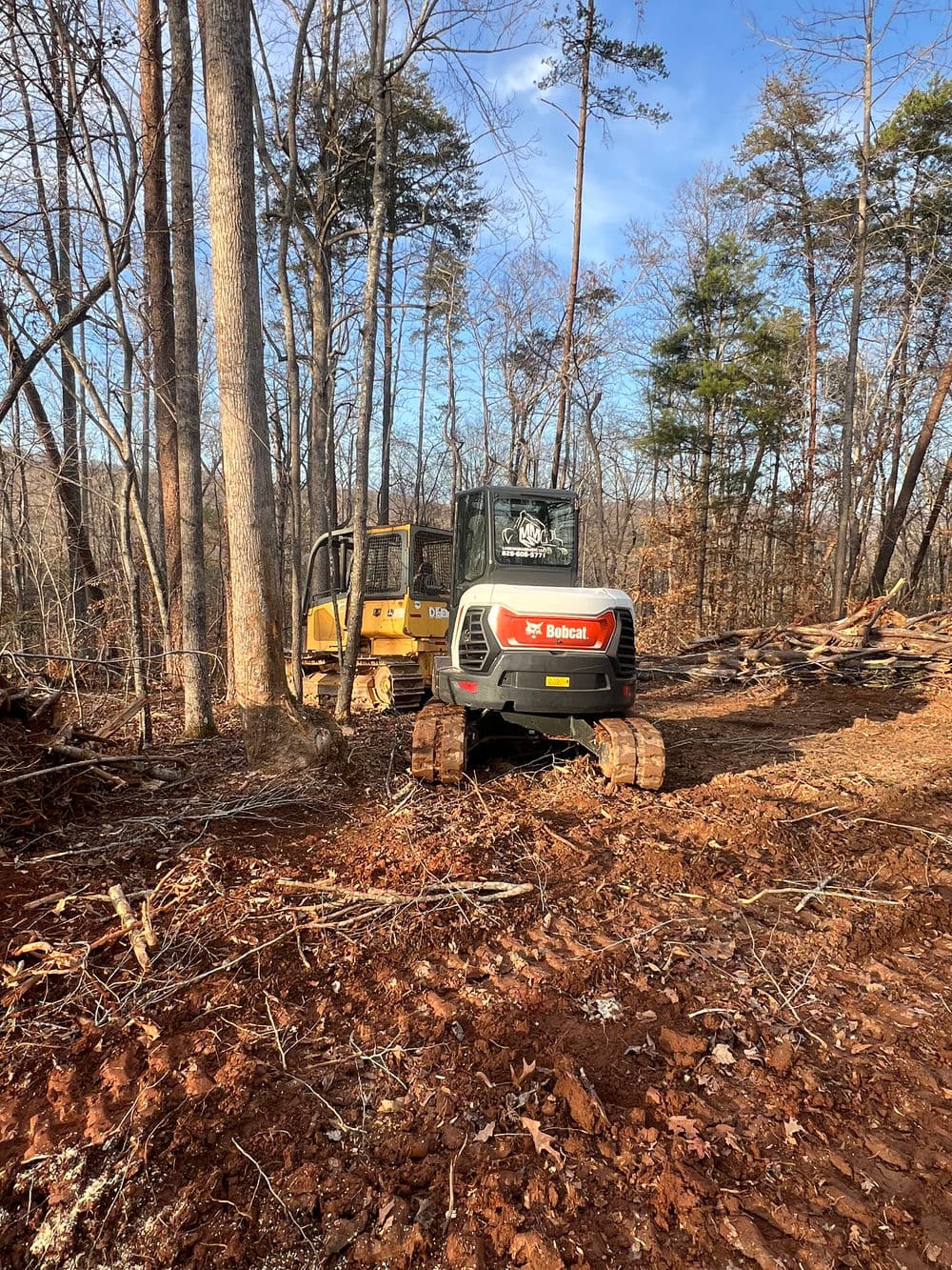 Excavators working in a wooded area, clearing land for construction or development.