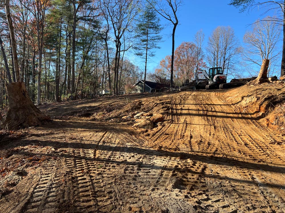 Cleared land with tire tracks, heavy machinery, and trees surrounding the area in autumn.