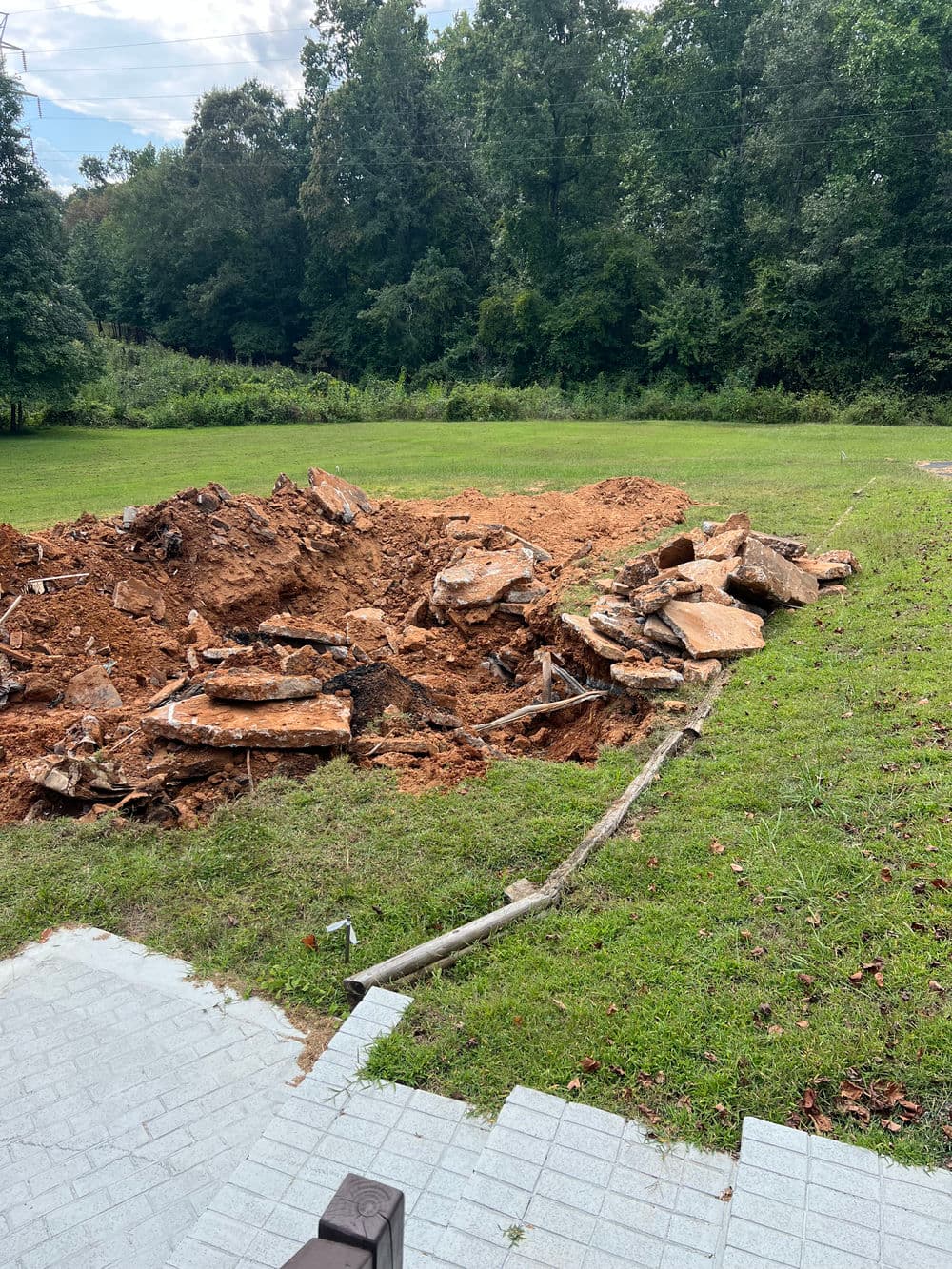Excavated land with large rocks and debris near a grassy area and stone pathway.
