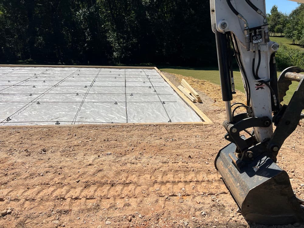 Construction site with a prepared concrete slab and excavator, surrounded by nature.
