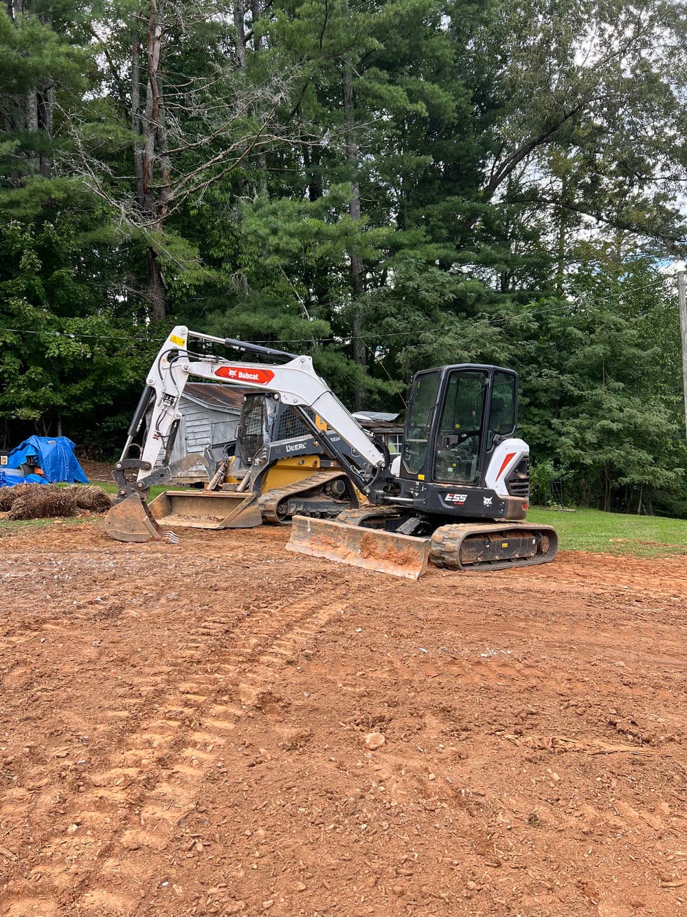 Excavators parked on a cleared construction site surrounded by trees and equipment.